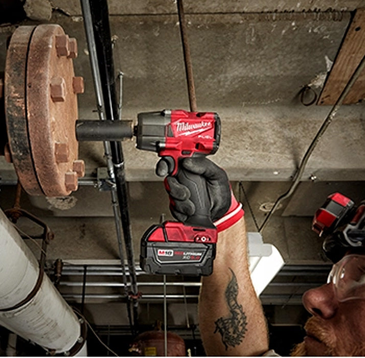 M18 Fuel 1/2" Mid Torque Impact Wrench in use tightening a large rusty bolt on industrial machinery, held by a.