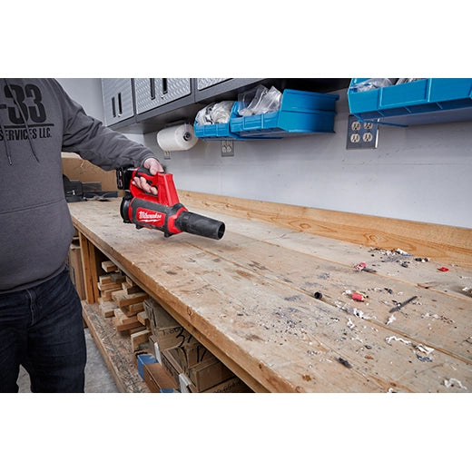 Milwaukee M12 Compact Blower 0852-20 red and black cordless tool clearing debris on wooden workbench with tools in.