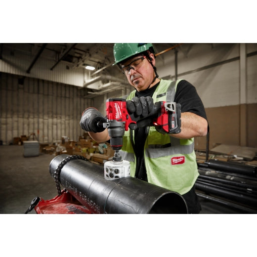 Milwaukee M18 Brushed 1/2 Hammer Drill 2904-20 cordless power tool being used on black pipe by worker in green vest .