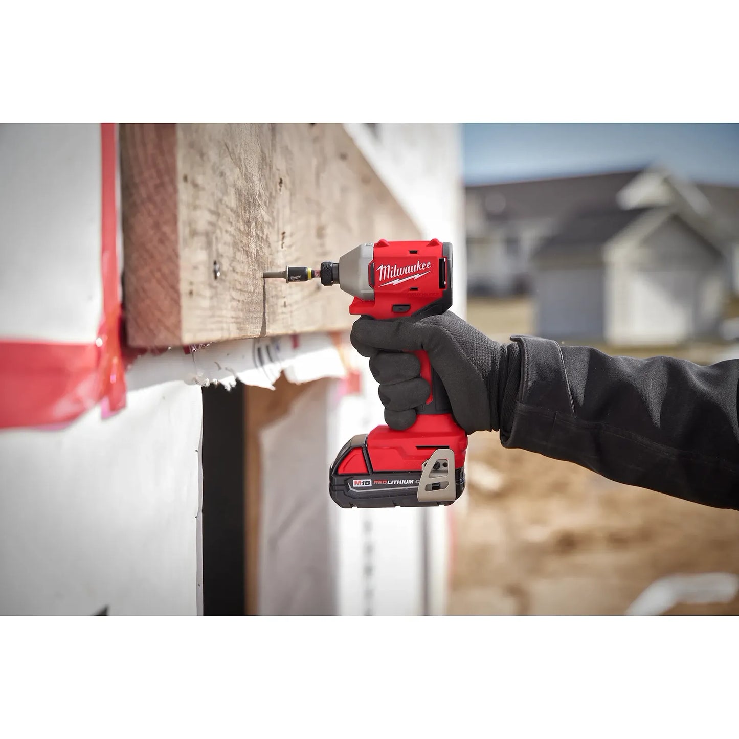 Milwaukee M18 Brushless 1/4 Impact Driver 3650-20 red and black tool in hand driving a screw into wood at a.