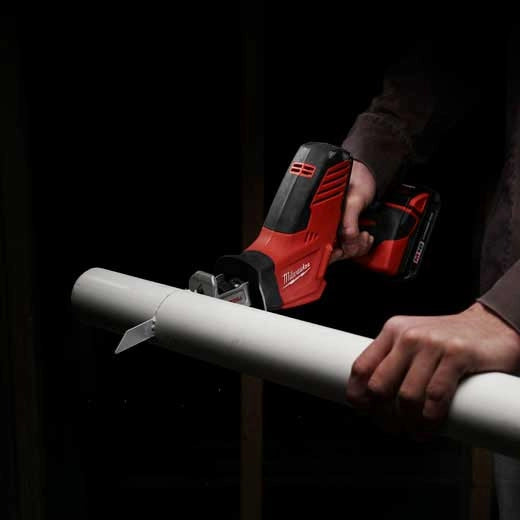 Milwaukee M18 Hackzall 2625-20 red cordless reciprocating tool cutting white PVC pipe held by hands tools.